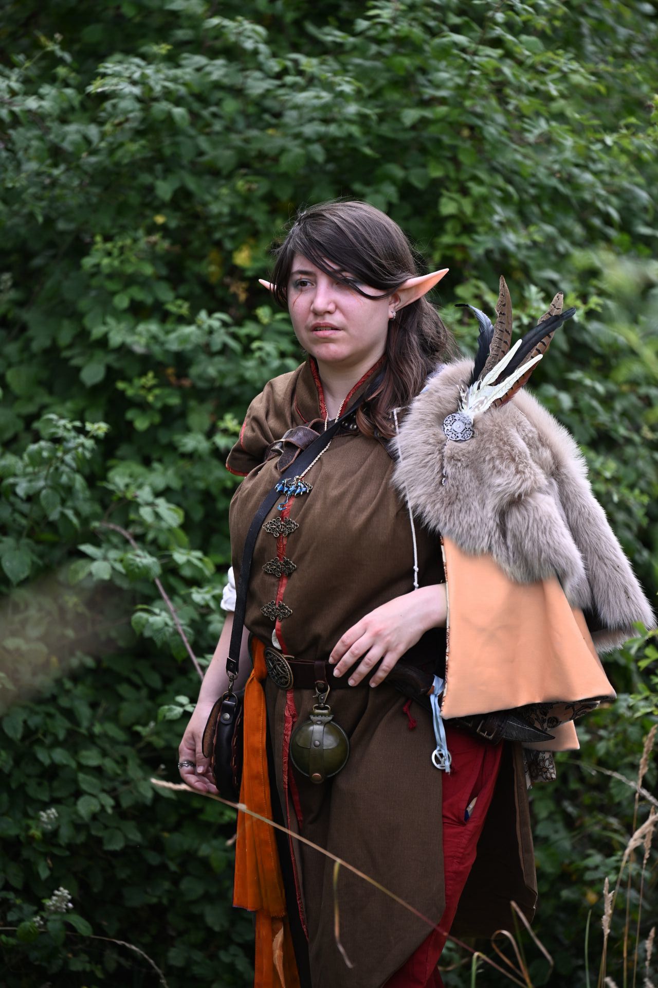 Chasseuse d'Avarosk : tabard marron, fourrure grise sur l'épaule, doublure rouge, pantalon rouge, foulard orange à la ceinture